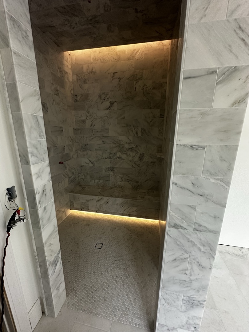 Custom marble shower bench with hex floor and LED cove lighting by KV Tileworks