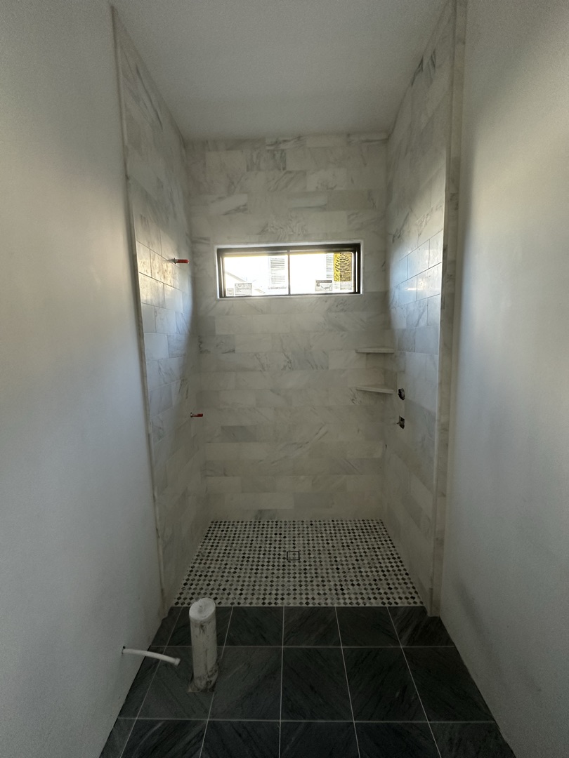 Marble wall shower with contrasting dark hex floor tile by KV Tileworks