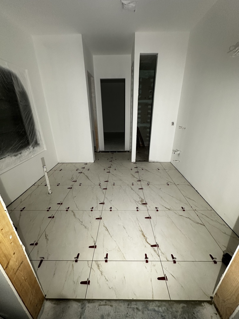 Large-format marble porcelain floor being set with leveling clips on a new construction build by KV Tileworks